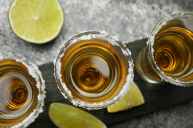 Photo of Mexican Tequila shots, lime slices and salt on grey table, top view