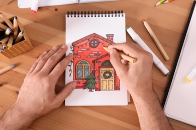 Photo of Man drawing in sketchbook with pencil at wooden table, top view