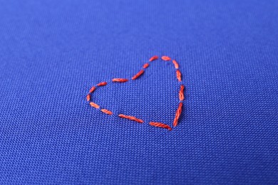 Photo of Red embroidered heart on blue cloth, closeup