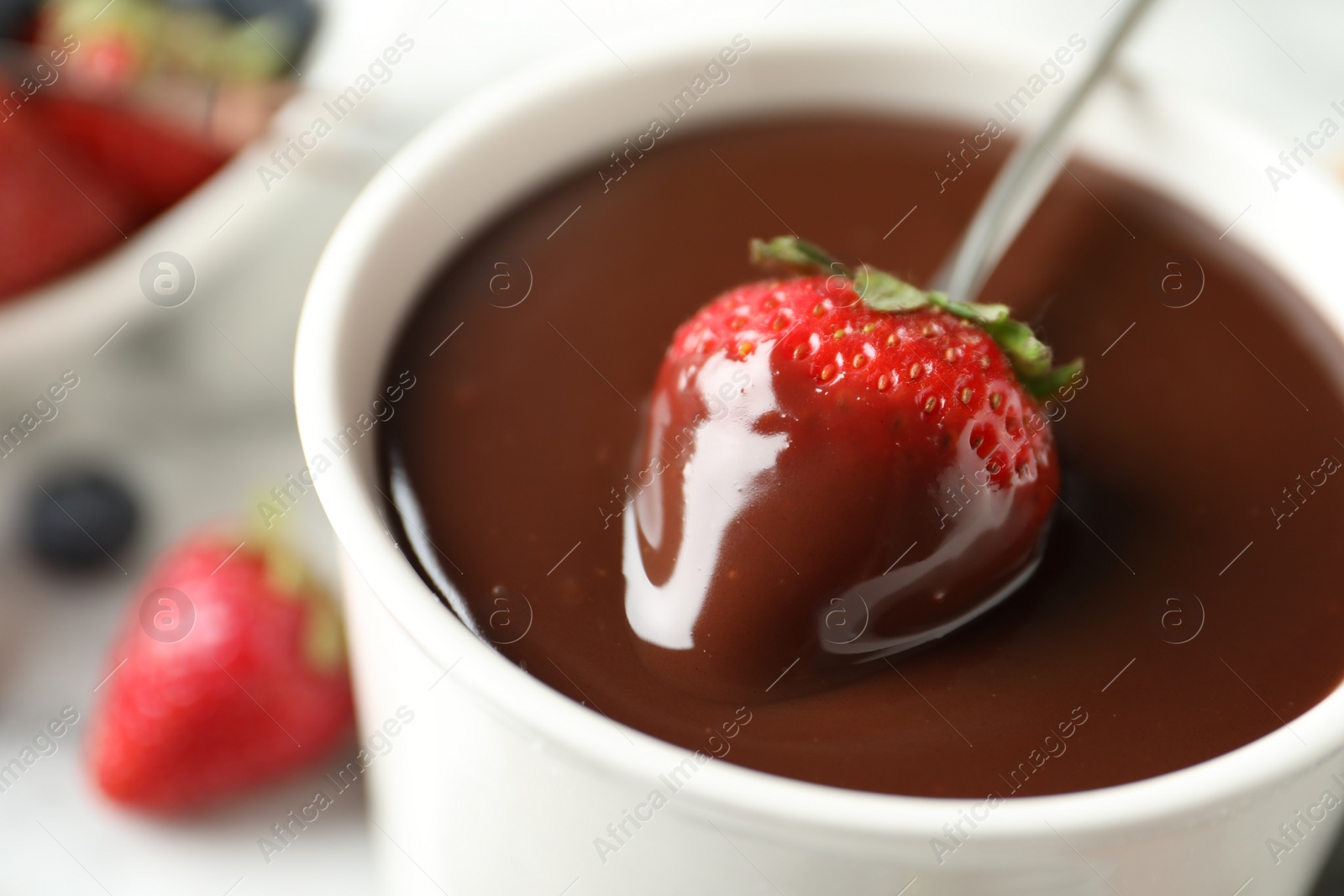 Photo of Dipping strawberry into fondue pot with chocolate, closeup