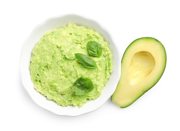 Bowl of tasty guacamole with basil and cut avocado on white background, top view