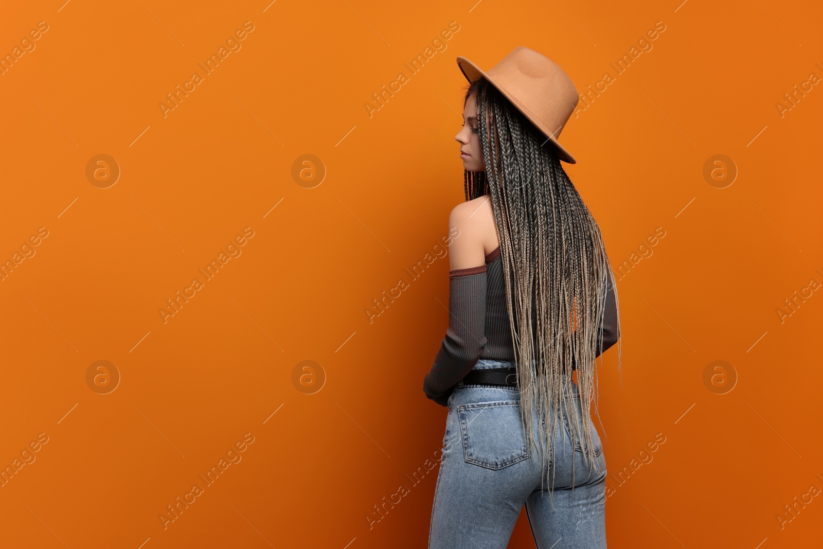 Photo of Beautiful woman with long african braids and hat on orange background, space for text