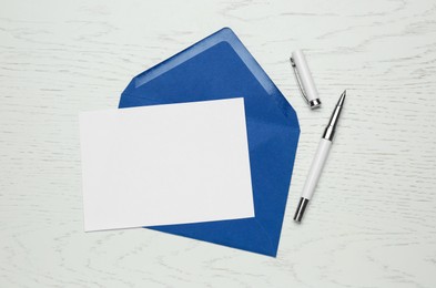 Photo of Envelope with blank paper card and pen on white wooden table, flat lay