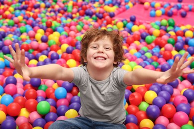 Photo of Happy little boy sitting on colorful balls in ball pit