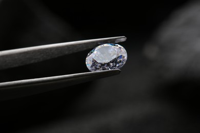 Photo of Tweezers with beautiful shiny diamond on dark background, closeup