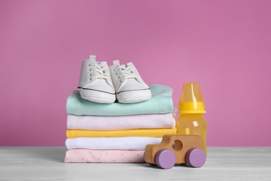 Photo of Children's shoes, stack of clothes and toy on white wooden table