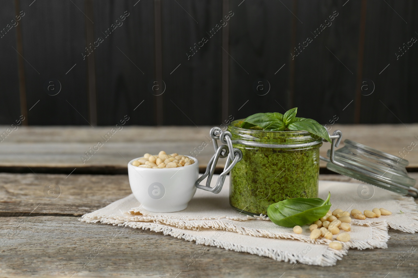 Photo of Delicious pesto sauce, pine nuts and basil leaves on wooden table. Space for text