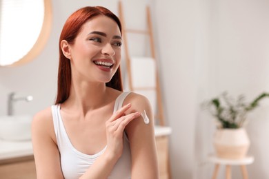 Photo of Beautiful young woman applying body cream onto shoulder in bathroom, space for text