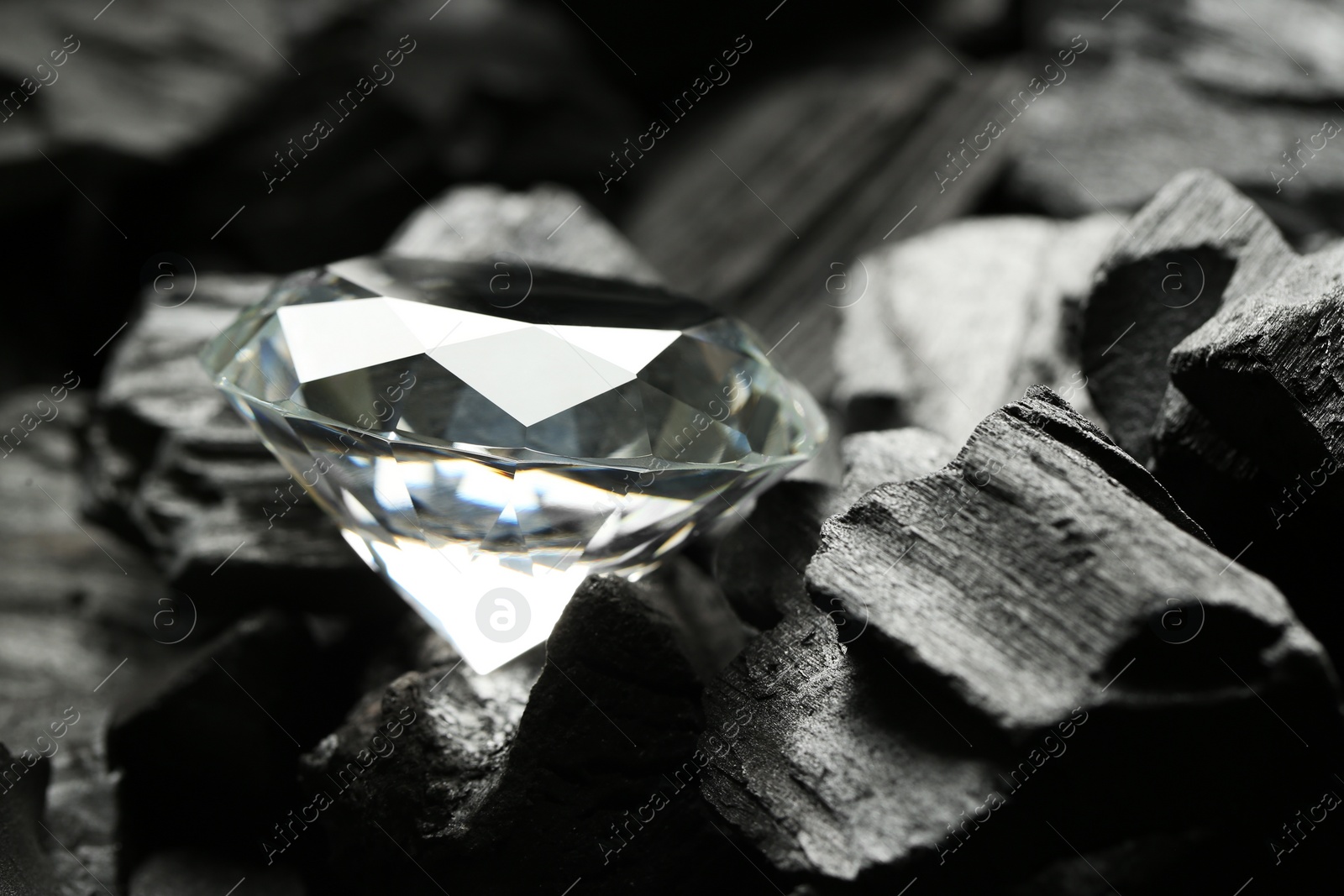 Photo of Beautiful shiny diamond on coals, closeup view