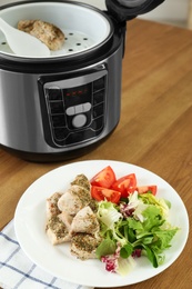 Photo of Delicious chicken with vegetables and modern multi cooker on wooden table