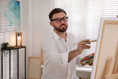 Photo of Young man painting on easel with brush in artist studio
