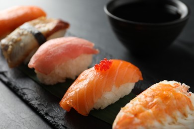 Photo of Serving board with delicious nigiri sushi and soy sauce on black table, closeup