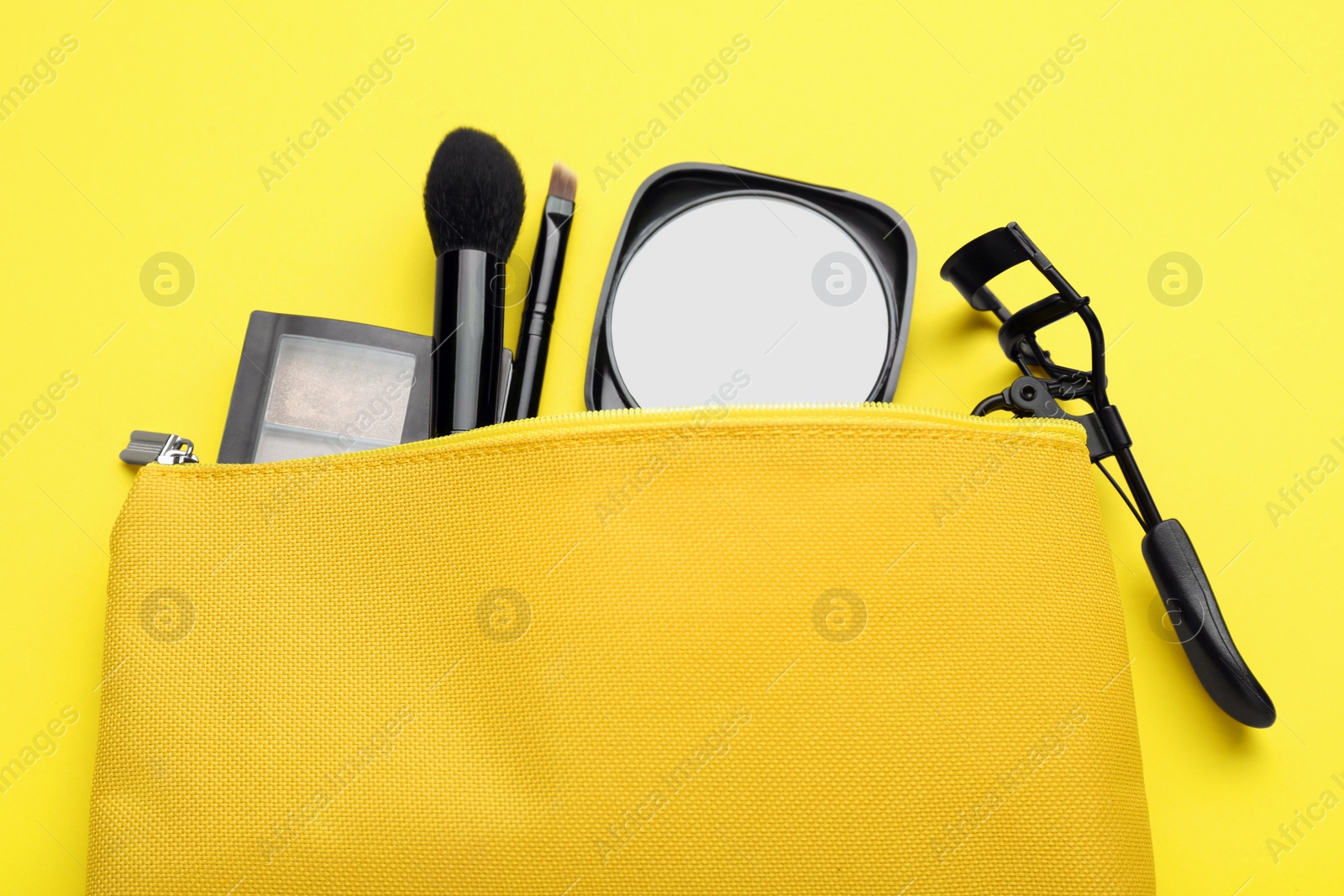 Photo of Cosmetic bag with pocket mirror and makeup products on yellow background, flat lay