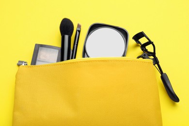 Cosmetic bag with pocket mirror and makeup products on yellow background, flat lay