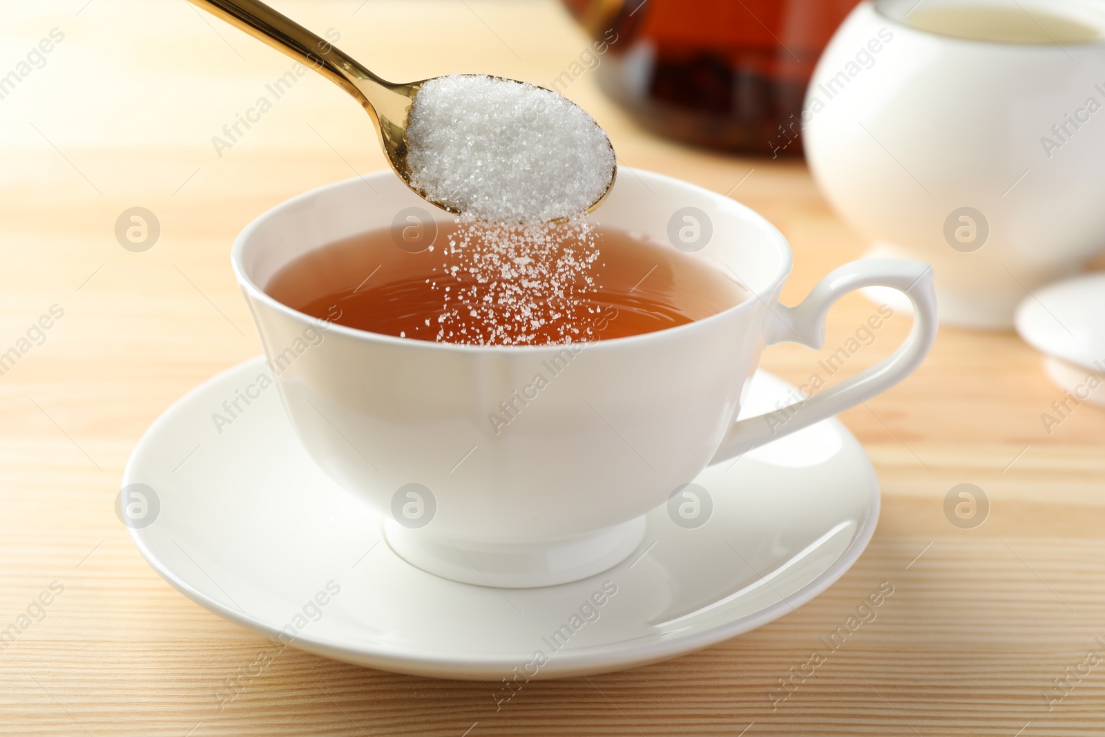 Photo of Adding sugar into cup of tea at wooden table, closeup