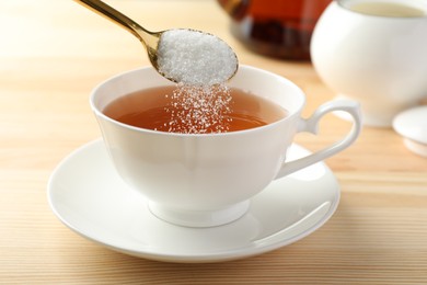 Adding sugar into cup of tea at wooden table, closeup