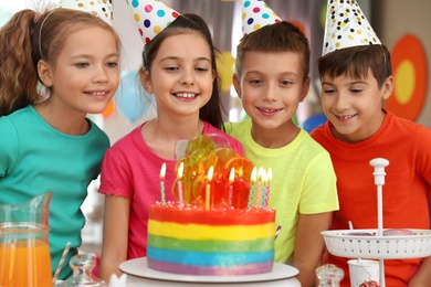 Photo of Children near cake with candles at birthday party indoors
