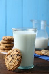 Photo of Delicious chocolate chip cookie and glass of milk on wooden table, closeup