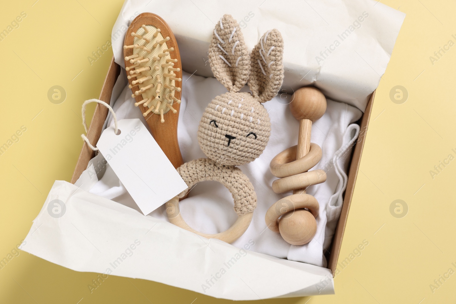 Photo of Different baby accessories and blank card in box on yellow background, top view