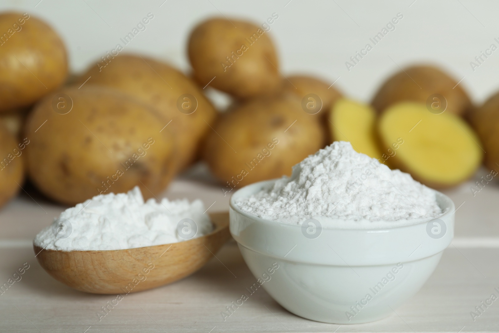 Photo of Starch and fresh raw potatoes on white wooden table, closeup