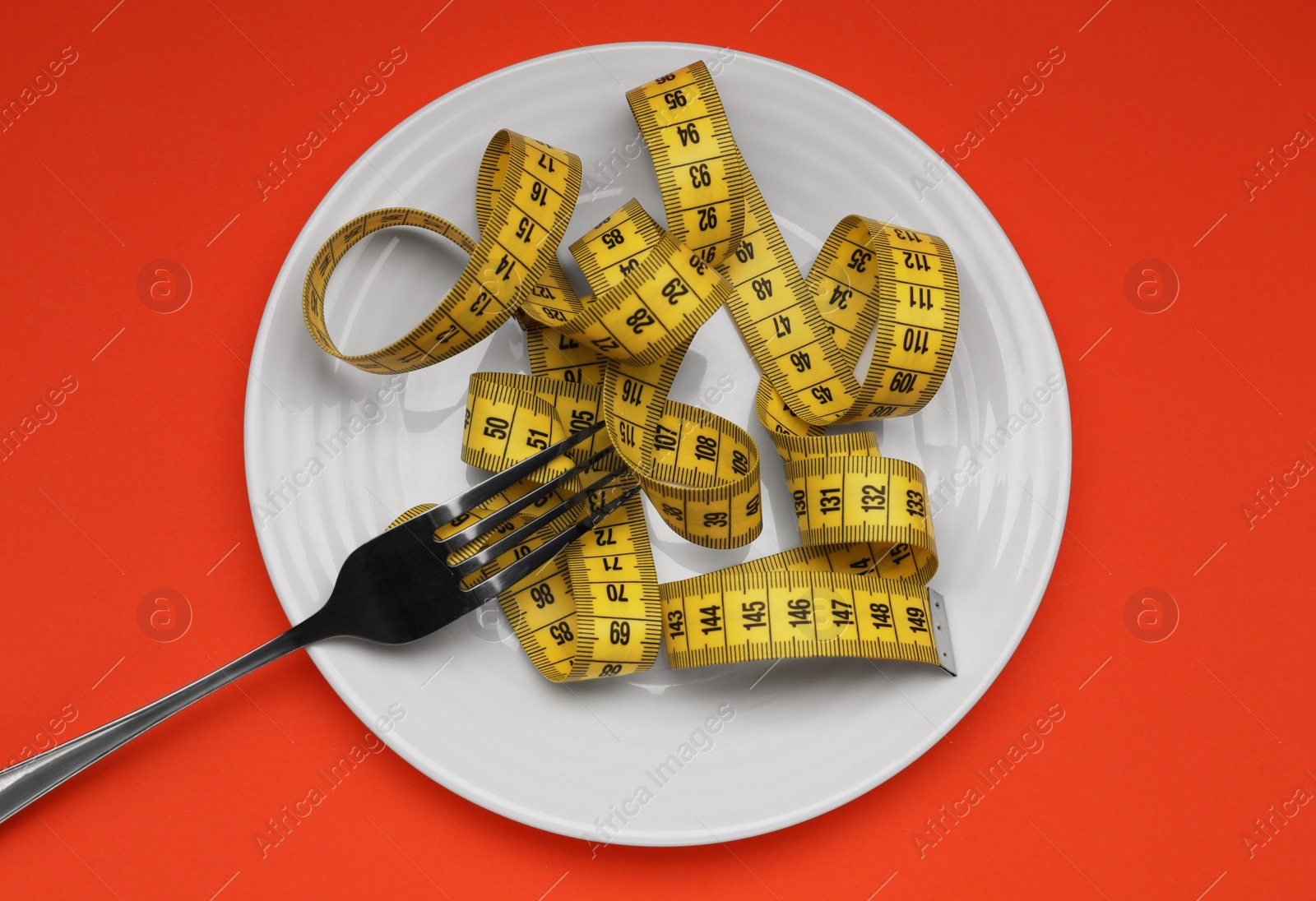 Photo of Plate, measuring tape and fork on red background, top view. Diet concept