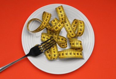 Photo of Plate, measuring tape and fork on red background, top view. Diet concept