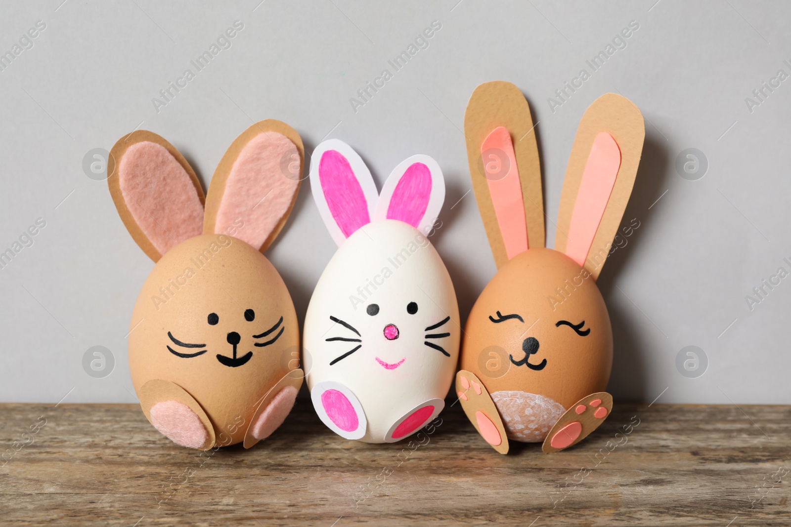 Photo of Eggs as cute bunnies on wooden table against light grey background. Easter celebration