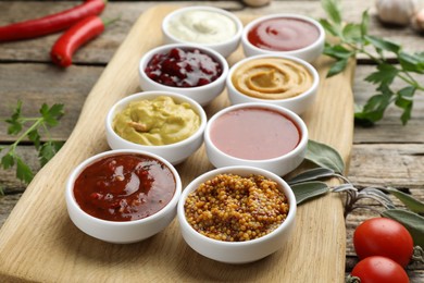 Different tasty sauces in bowls and ingredients on wooden table, closeup