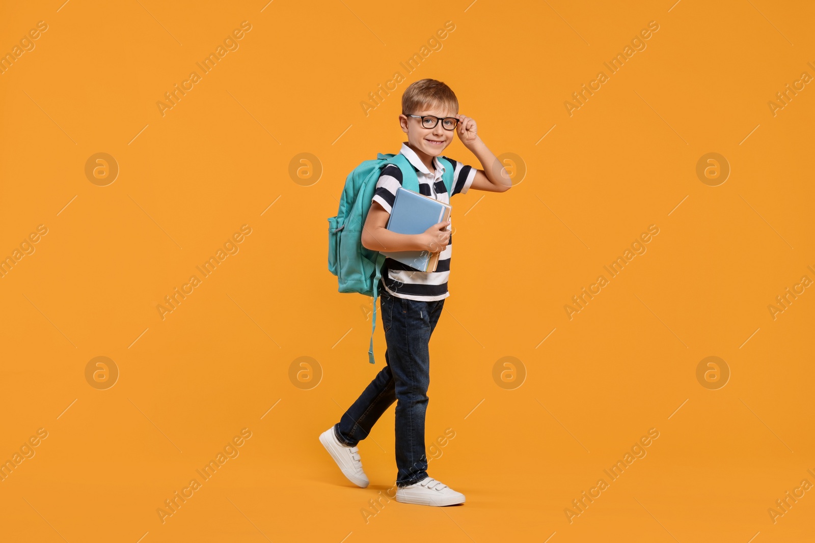 Photo of Happy schoolboy in glasses with backpack and books on orange background