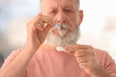 Photo of Senior man taking contact lens from container on blurred background