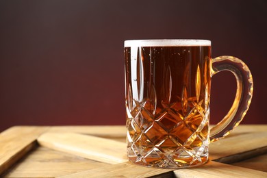 Photo of Mug with fresh beer on wooden crate against color background, closeup. Space for text
