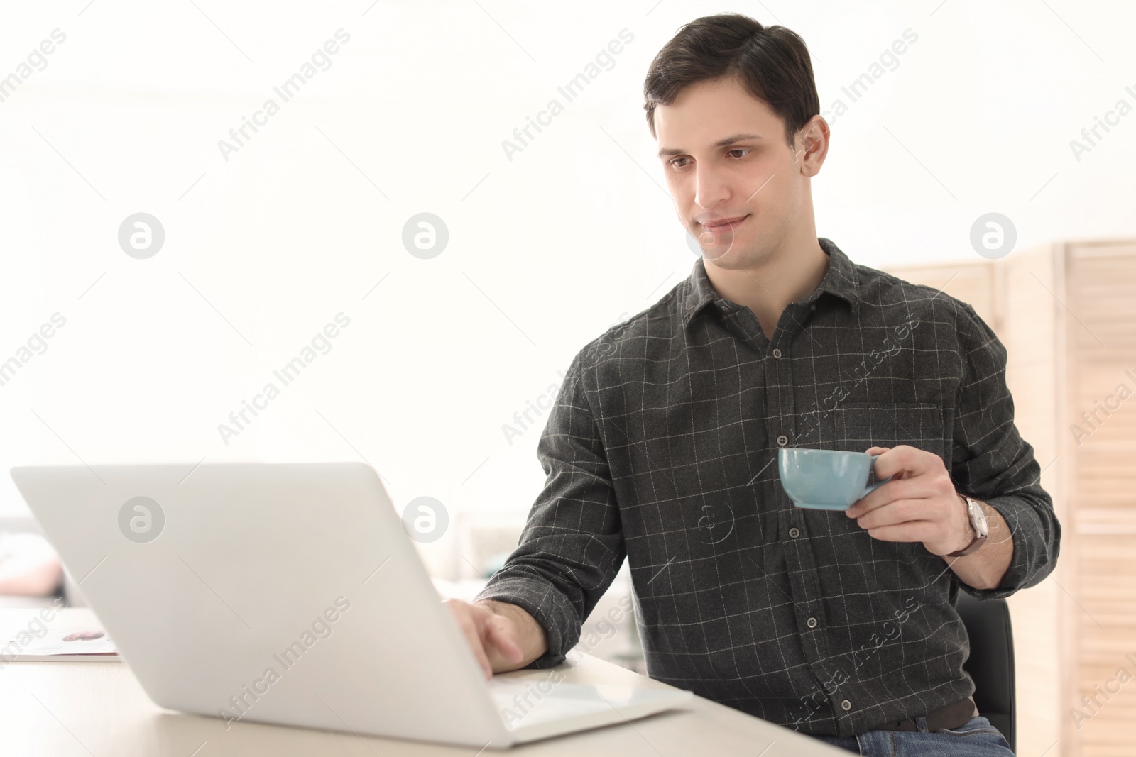 Photo of Portrait of confident young man with  laptop and cup at table