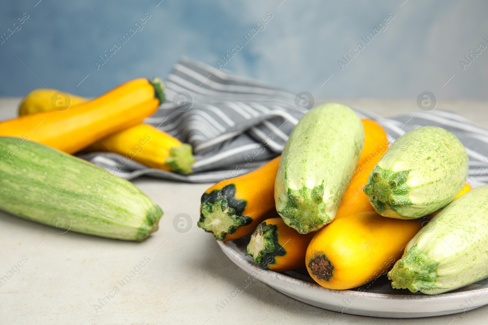Photo of Plate with fresh ripe zucchinis on light table against blue background, space for text