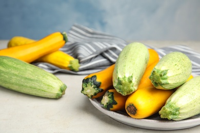 Plate with fresh ripe zucchinis on light table against blue background, space for text