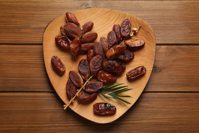 Photo of Branch with sweet dried dates and green leaf on wooden table, top view