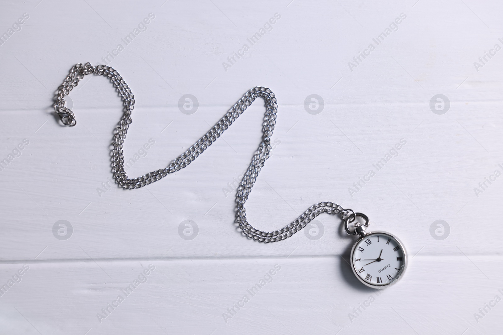 Photo of Silver pocket clock with chain on white wooden table, top view