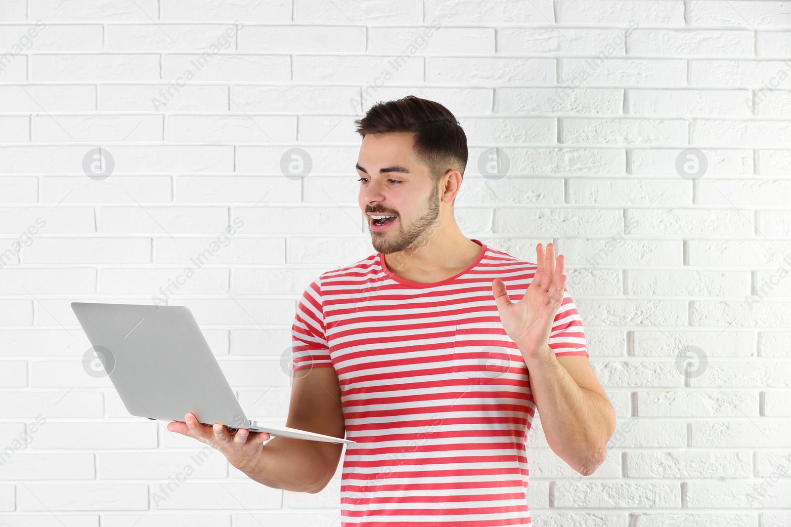 Photo of Man using laptop for video chat against brick wall