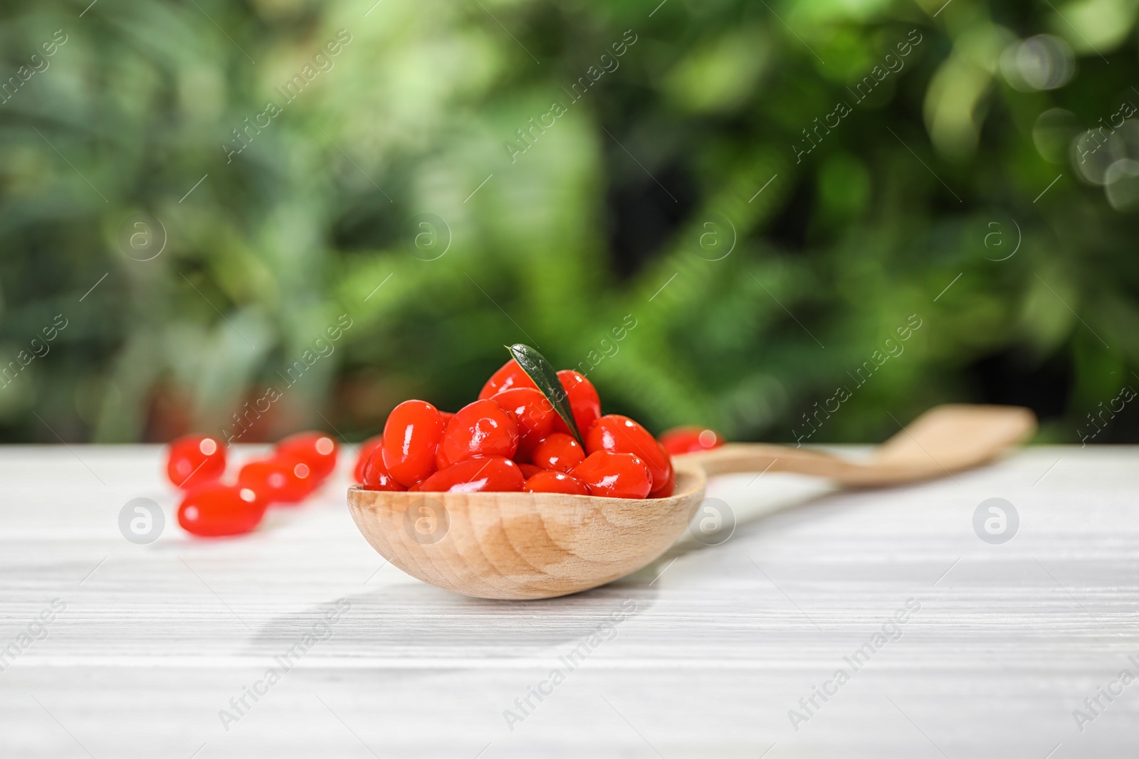 Photo of Spoon with fresh goji berries on white wooden table against blurred background. Space for text