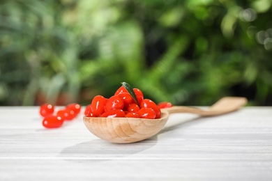 Photo of Spoon with fresh goji berries on white wooden table against blurred background. Space for text