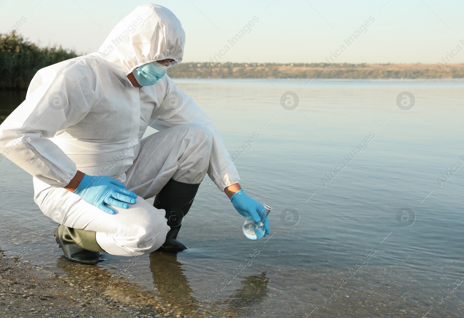 Photo of Scientist in chemical protective suit with florence flask taking sample from river for analysis