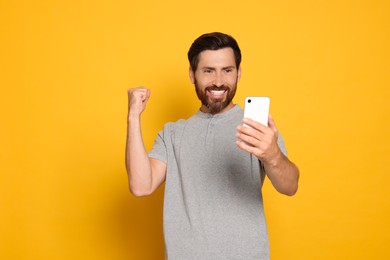 Emotional man looking at smartphone on yellow background