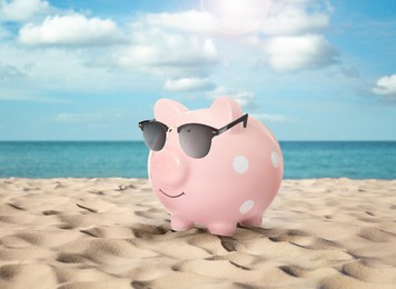 Image of Vacation savings. Piggy bank with sunglasses on sandy beach near sea