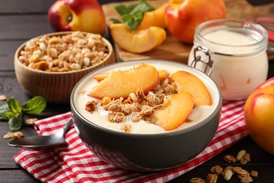 Photo of Tasty peach yogurt with granola and pieces of fruits in bowl on wooden table