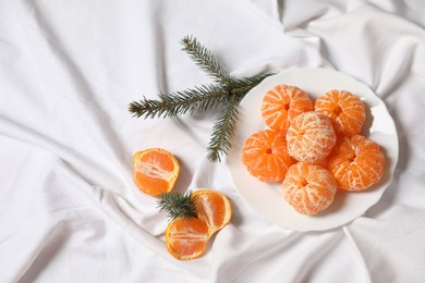 Photo of Peeled delicious ripe tangerines and fir branches on white bedsheet, flat lay. Space for text