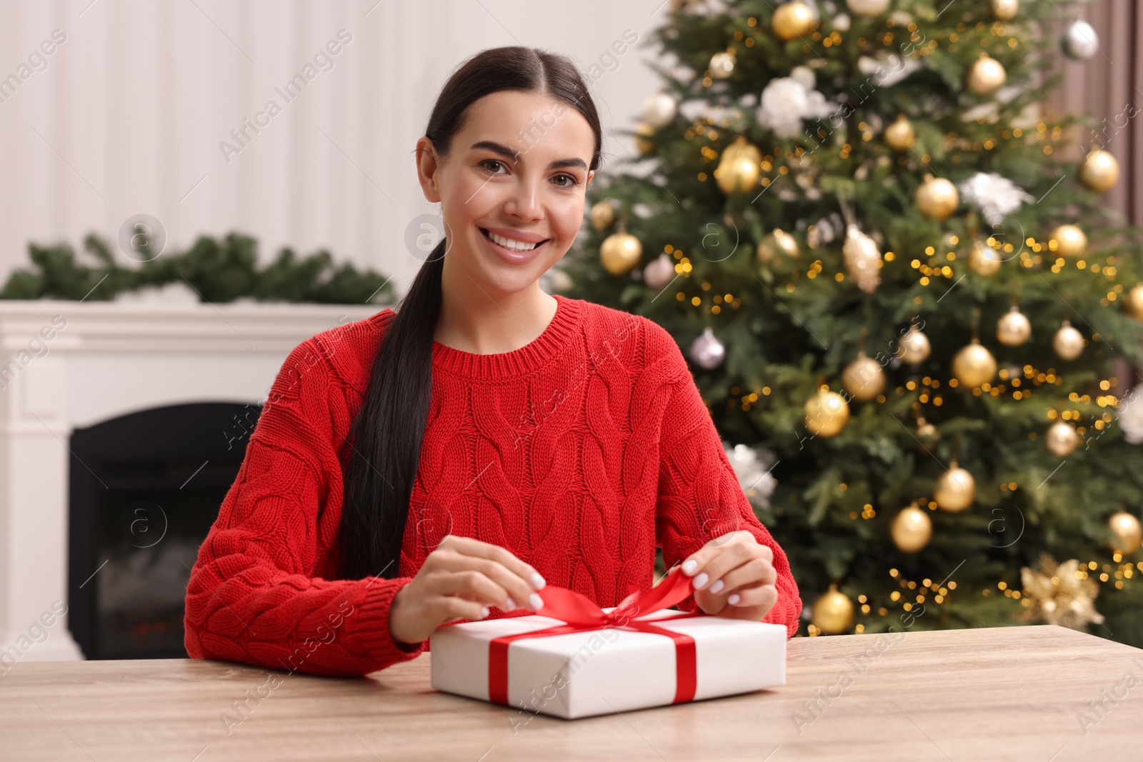 Photo of Happy woman opening Christmas gift at wooden table in room