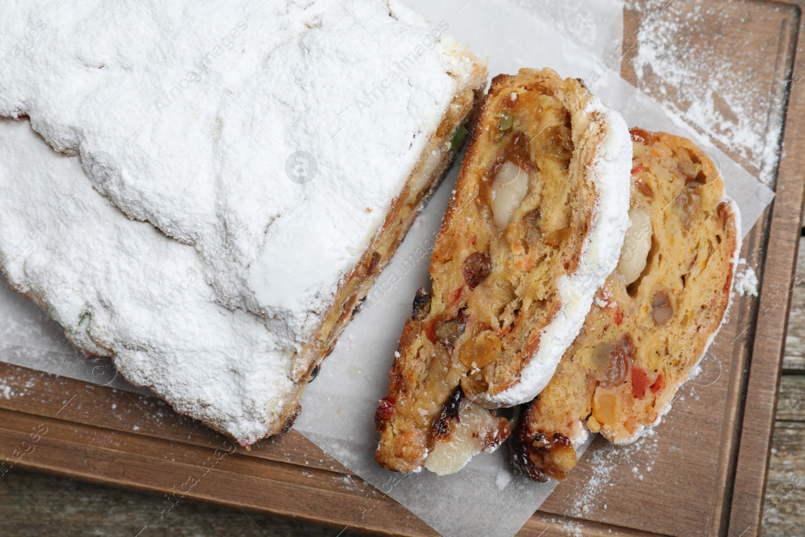 Photo of Traditional Christmas Stollen with icing sugar on wooden board, top view