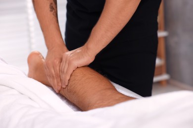 Man receiving professional leg massage on couch in spa salon, closeup