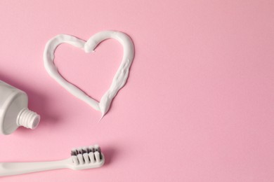Photo of Heart made with toothpaste, tube and brush on pink background, flat lay. Space for text
