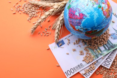 Photo of Import and export concept. Globe, ears of wheat and banknotes on orange background. Space for text