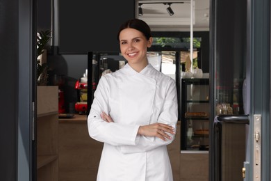 Happy baker in uniform at door of her cafe